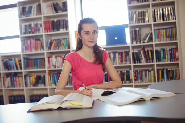 Schoolgirl doing homework in in in library at school — стоковое фото