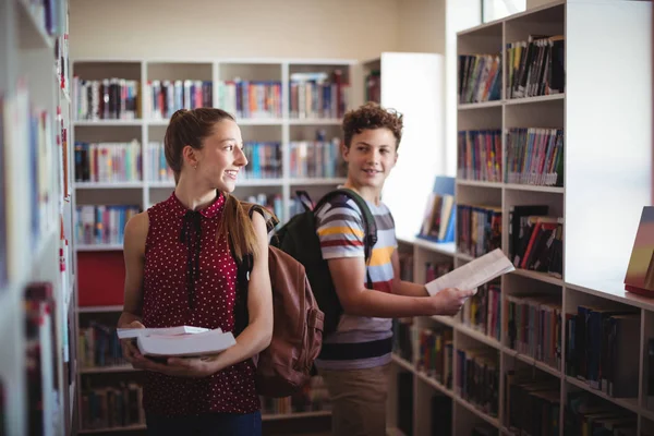 Classmates interacting while selecting book — Stock Photo, Image