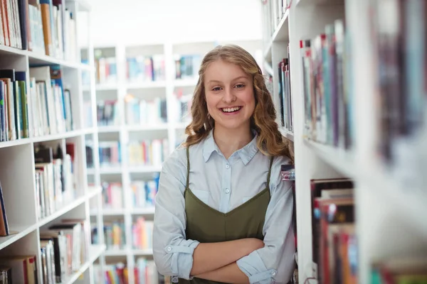 Skolflicka stående med armar korsade i biblioteket — Stockfoto