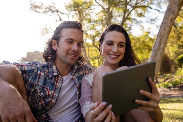 Couple sitting on grass and using tablet — Stock Photo, Image