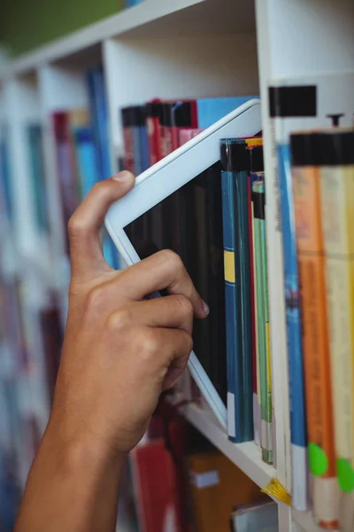 Estudante mantendo tablet na estante na biblioteca — Fotografia de Stock