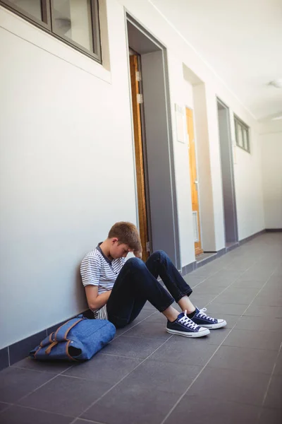 Sad schoolboy sitting in corridor — Stock Photo, Image