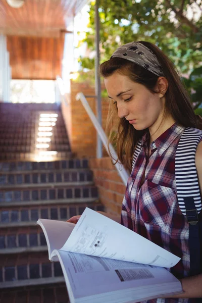 Attentive schoolgirl reading book near staircase — Stock Photo, Image