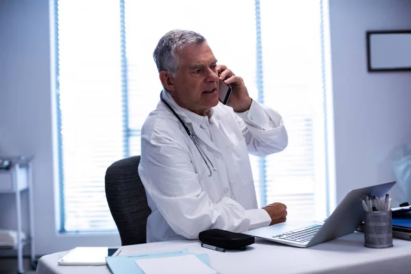 Doctor talking on phone while using laptop — Stock Photo, Image