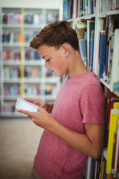Schooljongen via digitale tablet in bibliotheek — Stockfoto