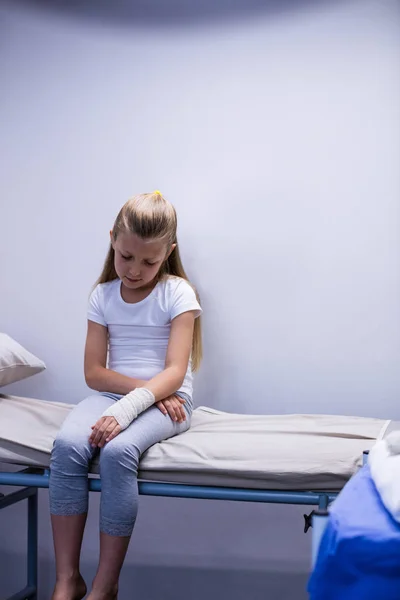 Meisje met gewonde hand zittend op bed brancard — Stockfoto