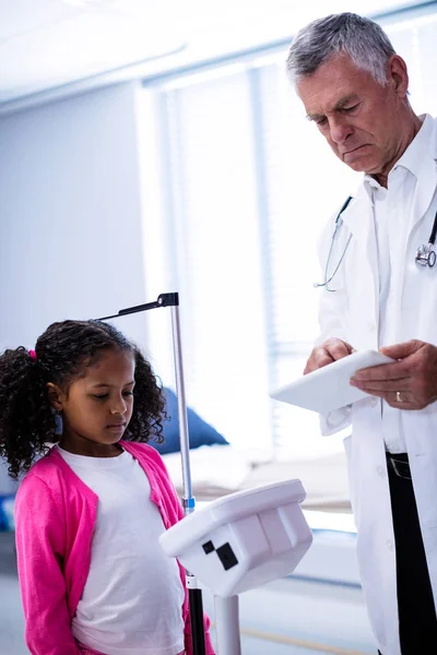 Arts met behulp van Tablet PC tijdens het meten van de hoogte van meisje — Stockfoto