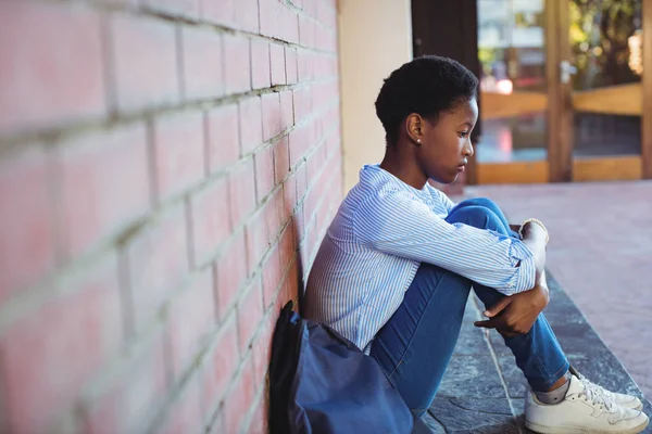 Sad schoolgirl sitting against brick wall — Stock Photo, Image