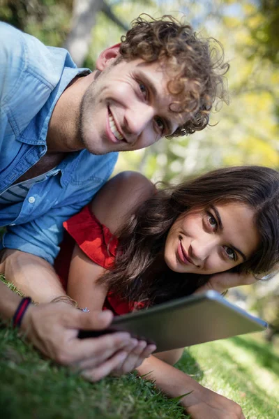 Para, leżąc na trawie i przy użyciu tabletu — Zdjęcie stockowe