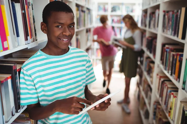 Schooljongen via digitale tablet in bibliotheek — Stockfoto