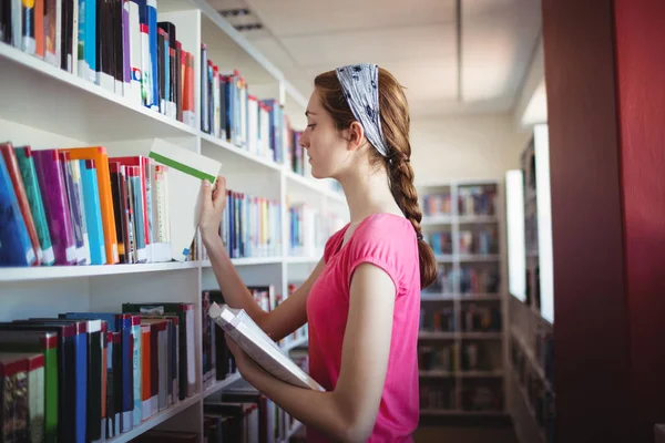 Colegiala seleccionar el libro de la estantería del libro —  Fotos de Stock