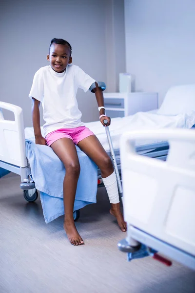 Girl with crutches sitting on hospital bed — Stock Photo, Image