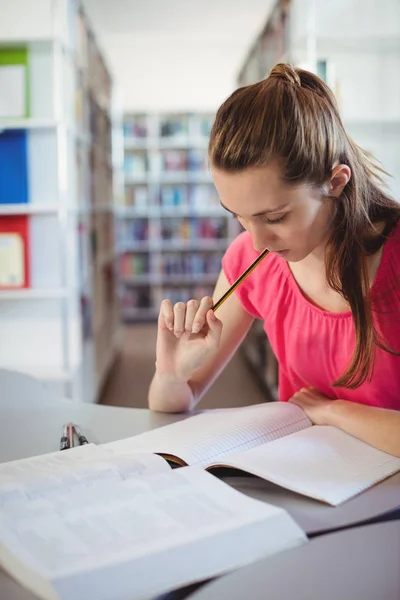 Schoolgirl doing homework in in in library — стоковое фото