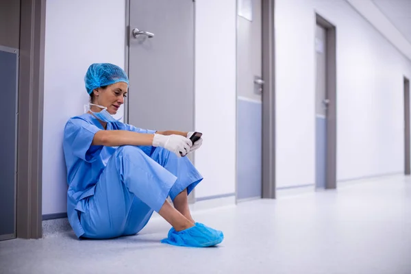 Surgeon sitting on floor and using phone — Stock Photo, Image