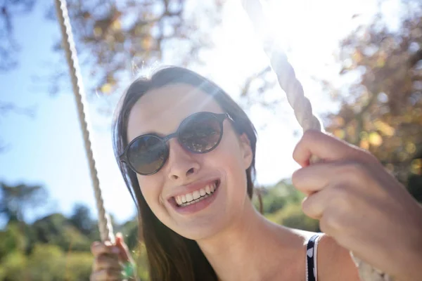 Leende kvinna som sitter på gunga i parken — Stockfoto