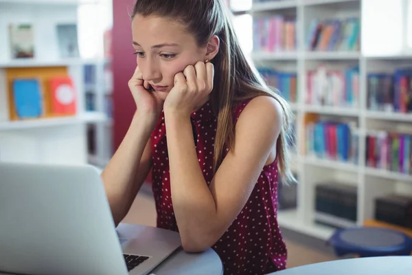 Smutny uczennica patrząc na laptopie w bibliotece — Zdjęcie stockowe