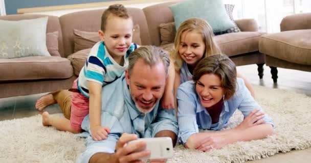 Szczęśliwa rodzina, leżąc na dywanie i rozmowy selfie na telefon komórkowy — Wideo stockowe