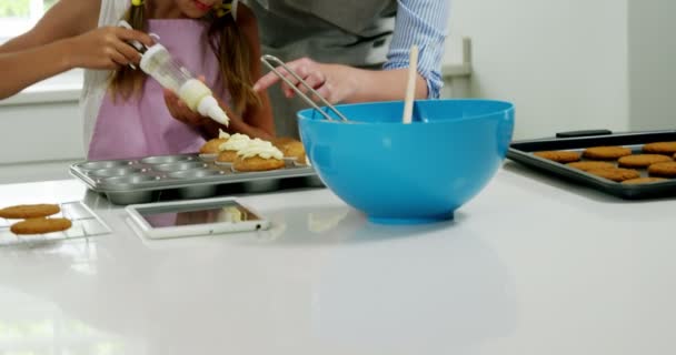 Мама помогает девушке украсить кекс кремом — стоковое видео