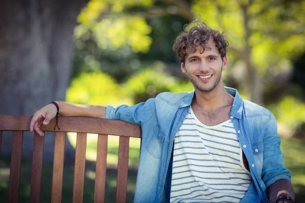 Homme souriant assis sur un banc dans le parc — Photo