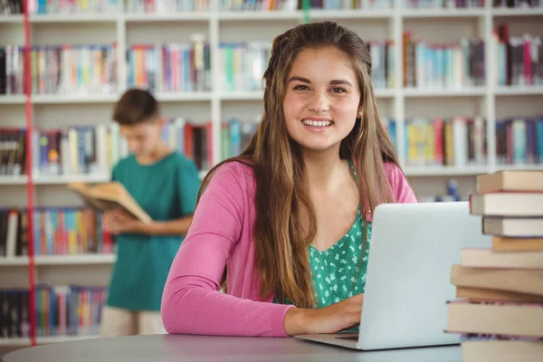 Porträtt av lycklig skolflicka med laptop i biblioteket — Stockfoto