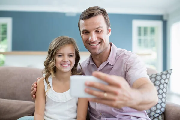 Ojciec i córka siedzi na kanapie i biorąc selfie — Zdjęcie stockowe