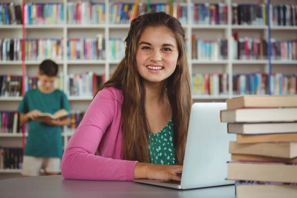 Retrato de colegial feliz usando laptop na biblioteca — Fotografia de Stock
