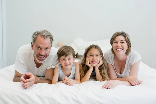 Портрет улыбающейся семьи лежащей на кровати — стоковое фото