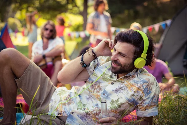 Man in headphones holding beer bottle at campsite — Stock Photo, Image