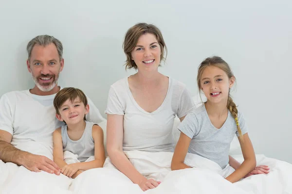 Семья, сидящая вместе на кровати в спальне — стоковое фото