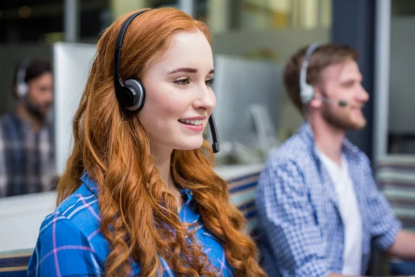 Lächelnde Kundendienstmitarbeiterin im Gespräch auf dem Headset am Schreibtisch — Stockfoto