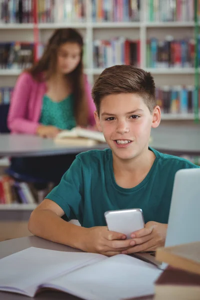Écolier souriant utilisant le téléphone portable dans la bibliothèque à l'école — Photo