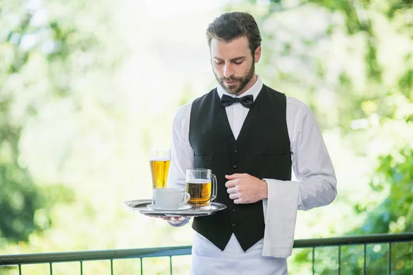 Garçom masculino segurando bandeja com copo de cerveja e xícara de café no restaurante — Fotografia de Stock