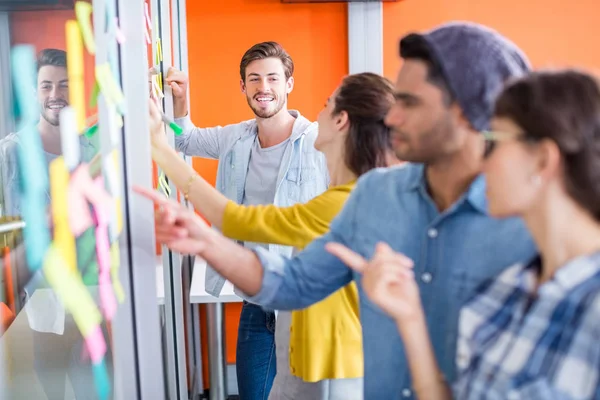 Smiling executives reading sticky notes on glass wall — Stock Photo, Image