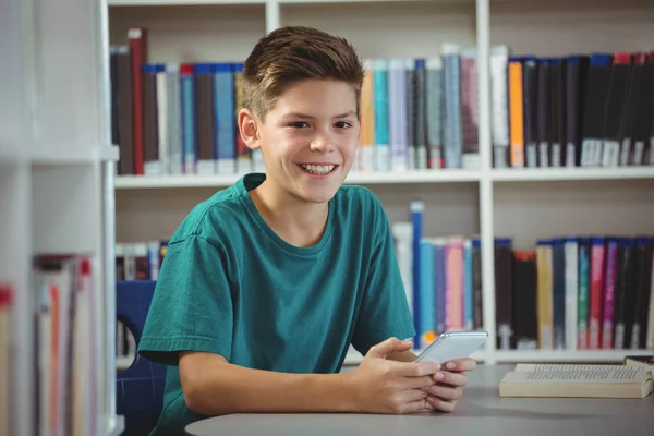 Lachende schooljongen gebruik mobiele telefoon in de bibliotheek op school — Stockfoto