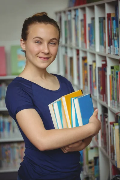 Porträtt av Skolflicka stående med trave böcker i biblioteket — Stockfoto