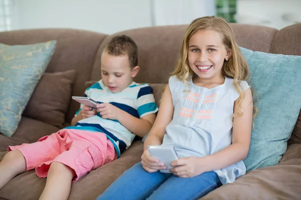 Sorella e fratello seduti sul divano utilizzando il telefono — Foto Stock