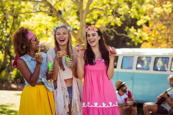 Happy friends blowing bubbles from bubble wand in park — Stock Photo, Image