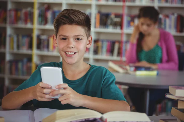 Leende skolpojke med mobiltelefon i biblioteket i skolan — Stockfoto