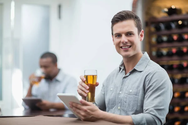 Schöner Mann hält Bierglas während er digitales Tablet benutzt — Stockfoto