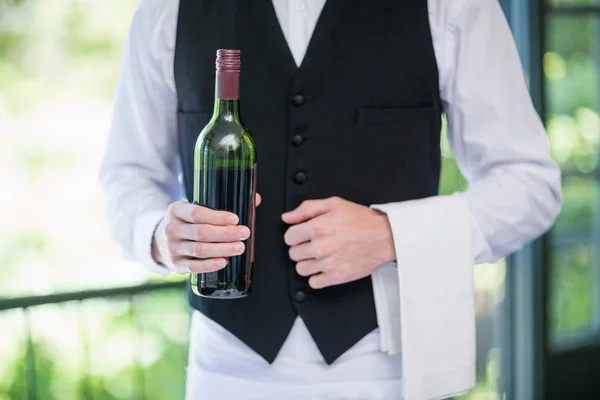 Male waiter holding bottle of wine in restaurant — Stock Photo, Image