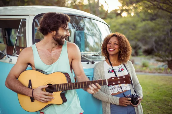 Mężczyzna gra na gitarze w pobliżu Kamper, podczas gdy kobieta stoi obok niego — Zdjęcie stockowe