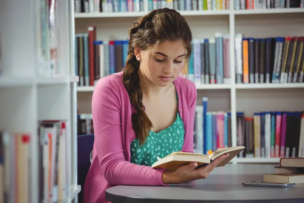 Attentive schoolgirl reading book in library — Stock Photo, Image