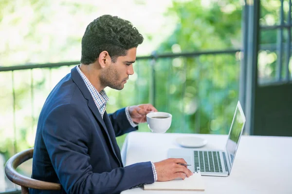 Homme d'affaires tenant tasse de café tout en utilisant un ordinateur portable — Photo