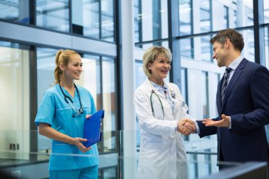 Female doctor shaking hands with businessman clipart