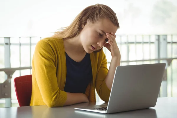 Triste colegiala mirando portátil en la biblioteca —  Fotos de Stock