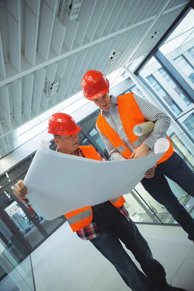 Male architects discussing over blueprint in corridor — Stock Photo, Image