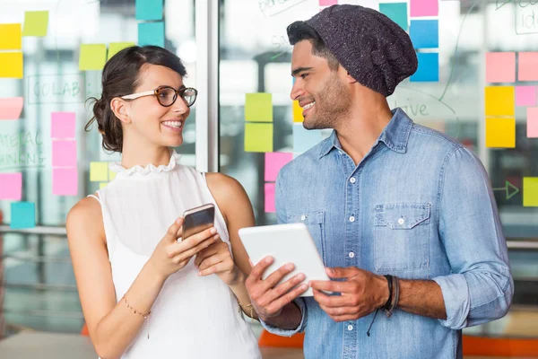 Ejecutivos sonrientes interactuando entre sí mientras usan teléfonos móviles y tabletas digitales — Foto de Stock