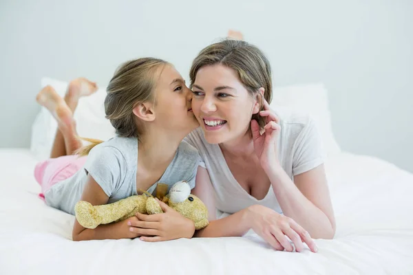 Adorable girl kissing her mother lying on bed — Stock Photo, Image