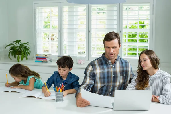 Батьки працюють з ноутбуком та дітьми, які навчаються — стокове фото