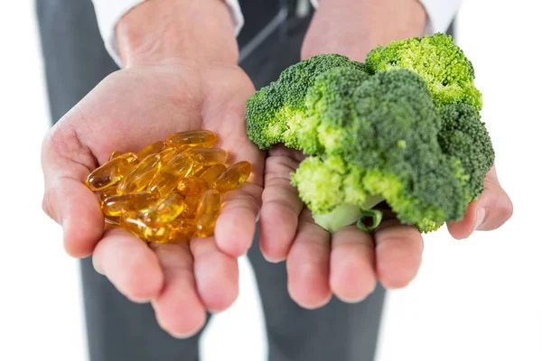 Empresário segurando brócolis e vitaminas — Fotografia de Stock